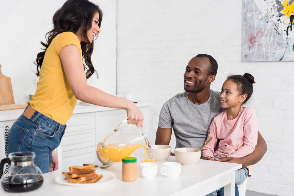 woman pouring orange juice into glass for husband and daughter woman pouring orange juice into glass for husband and daughter
