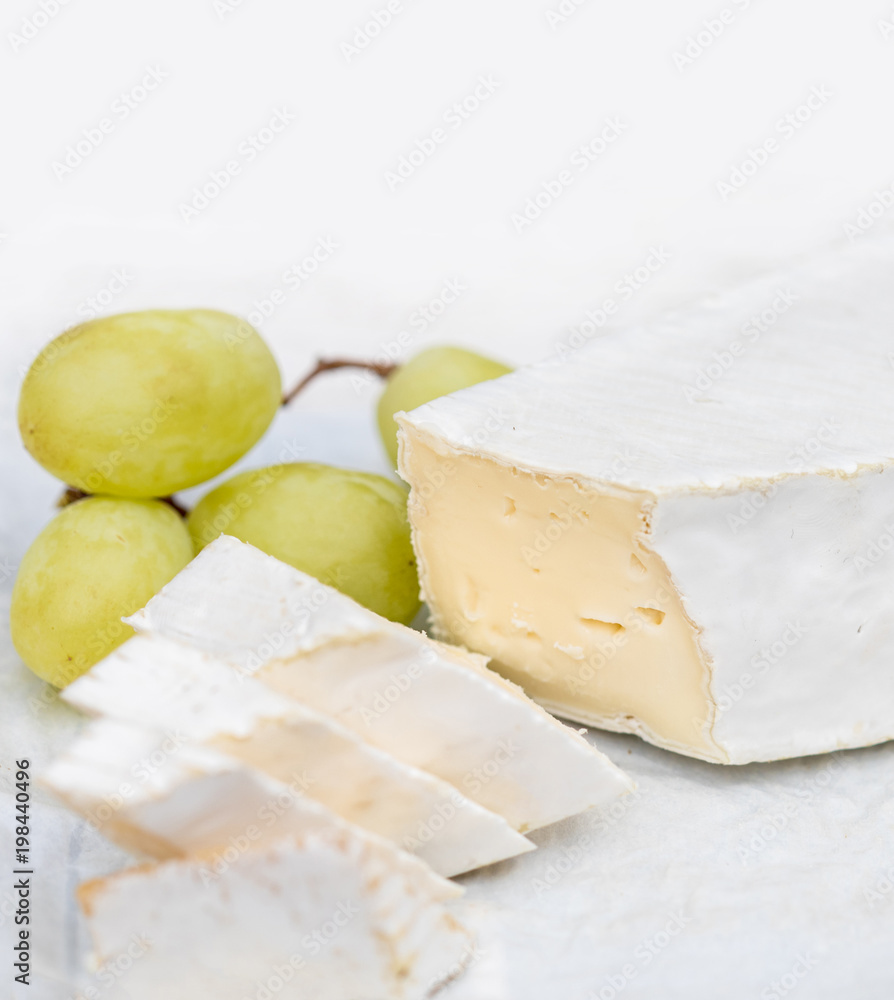 Fresh Brie cheese with slices and grape on white rustic on a wooden board. Brie type of cheese.  Camembert cheese.