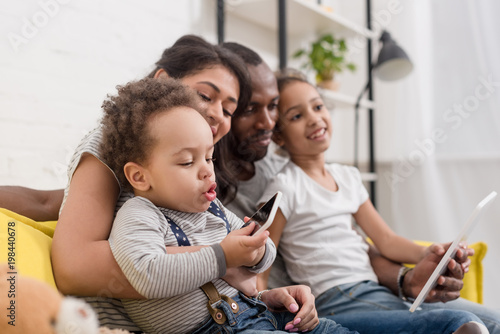 happy young family spending time together with devices on couch