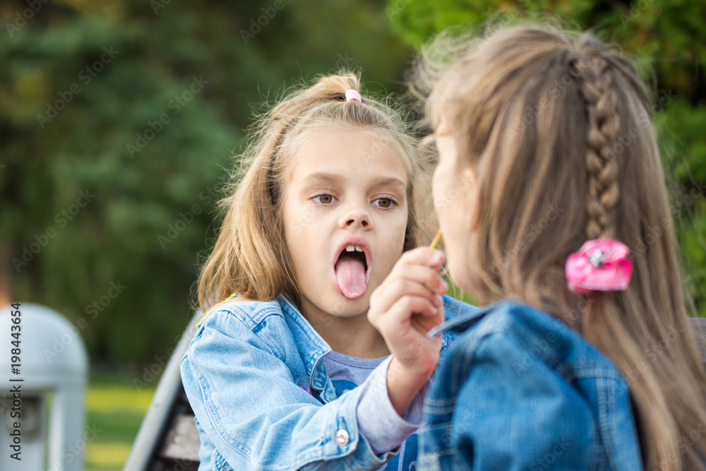 One girl treats another girl with her lollipop One girl treats another girl with her lollipop