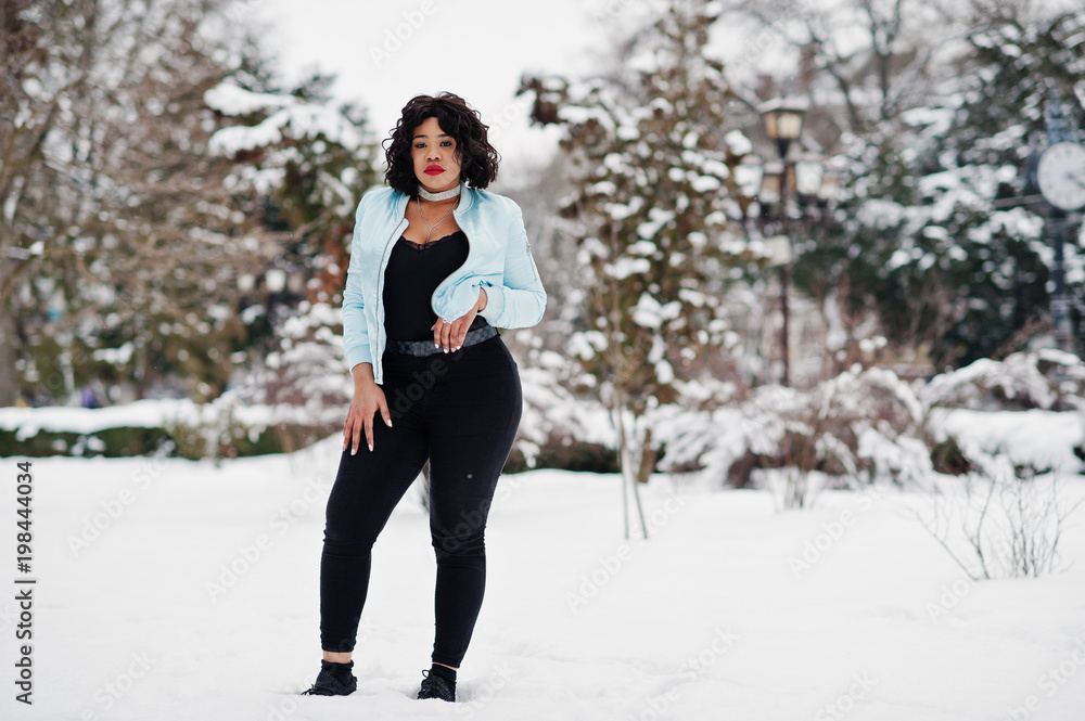 Stylish african american plus size model with mobile phone at hand  at winter snowy day.