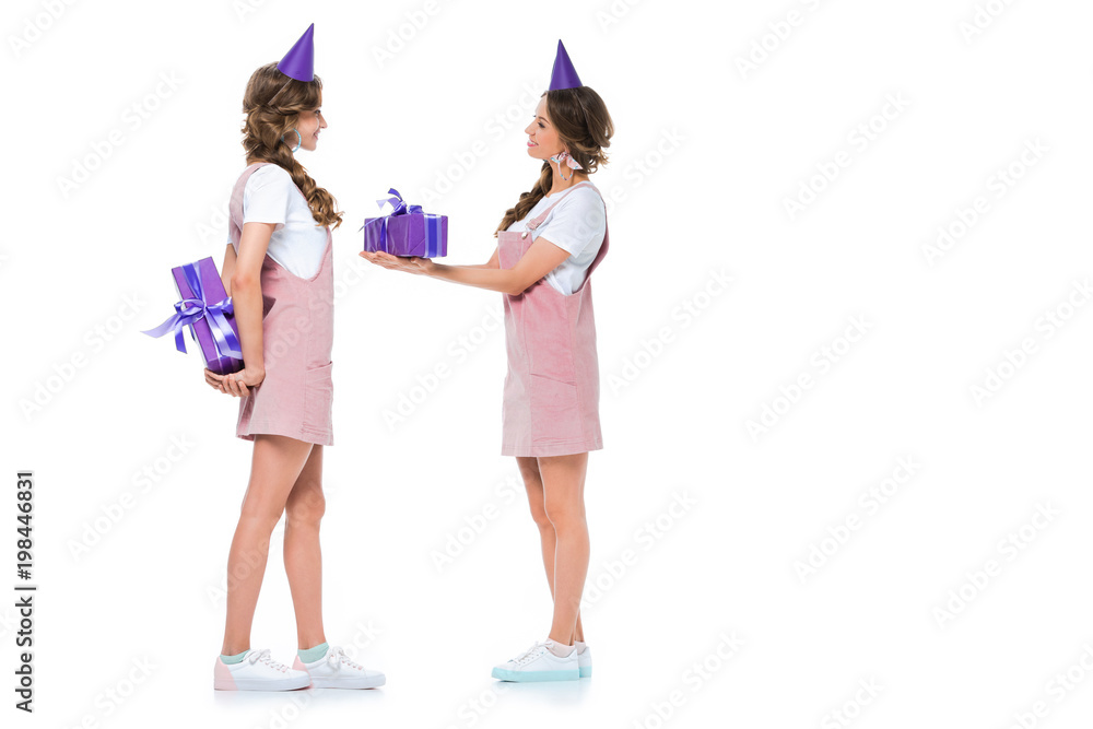 side view of beautiful young twins gifting each other presents isolated on white side view of beautiful young twins gifting each other presents isolated on white