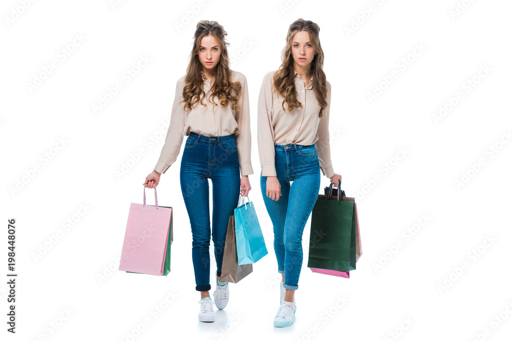 attractive young twins walking with shopping bags isolated on white