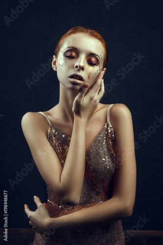 Beautiful model wearing golden dress is posing in a dark studio 