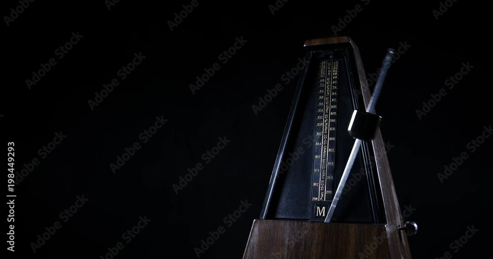 Slow motion shot of vintage metronome with golden pendulum beats slow rhythm on the dark background
