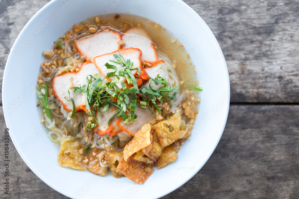 Close-up of Thai Noodle Soup with Meat in white bowl on wooden background.