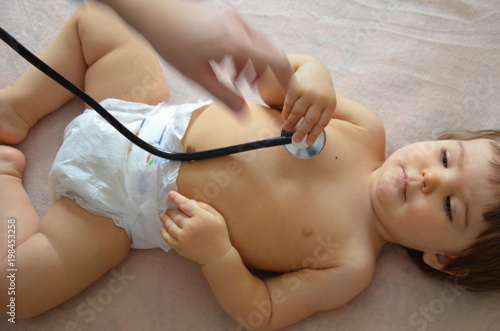 Pediatrician examining baby girl. Doctor using stethoscope to listen to kid back checking heart beat.