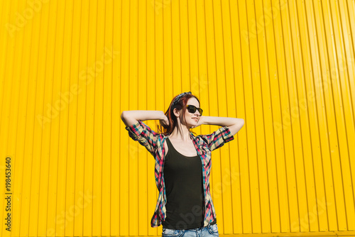 Redhead girl in denim shorts and pantyhose mesh is listening music with headphones on yellow background photo