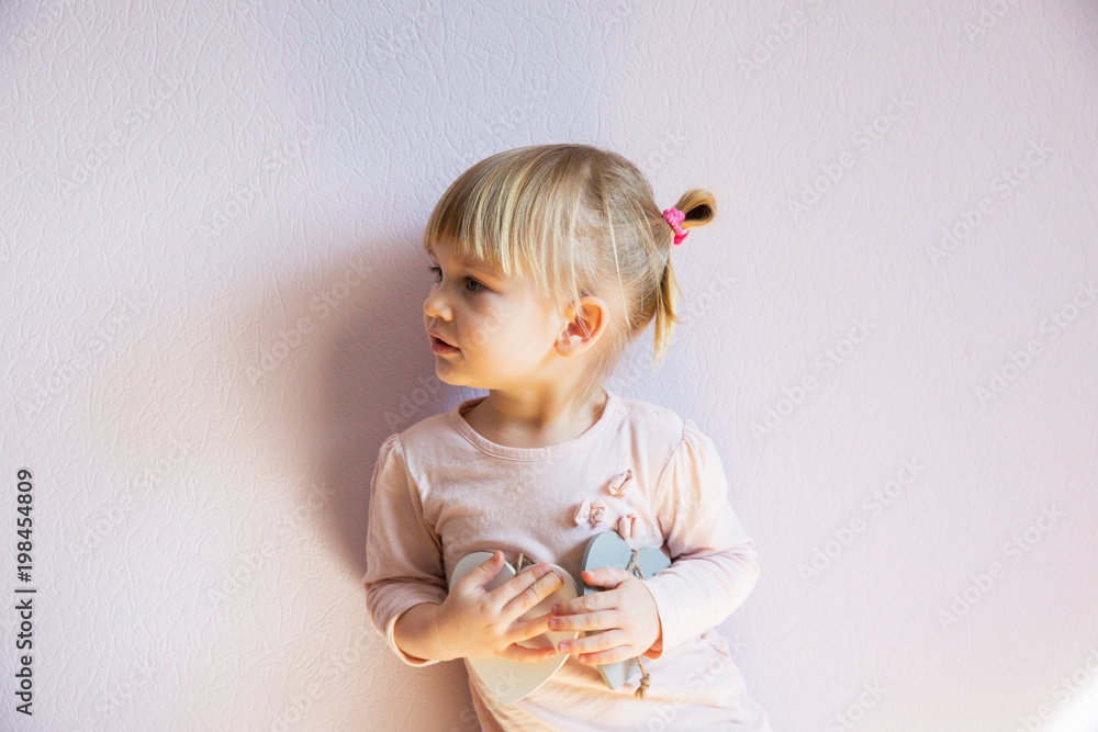 A serious little girl. A little girl with blond hair holds two wooden white hearts in her hands. It is thoughtful and serious. A serious little girl. A little girl with blond hair holds two wooden white hearts in her hands. It is thoughtful and serious.