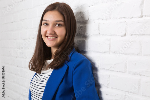 A young pretty smiling girl against a white loft-style brick wall. She looks at the viewer. Copy space. photo