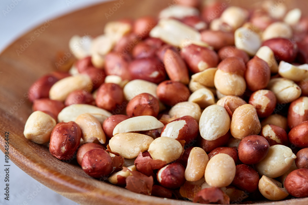 Raw mixed peanuts in wooden plate isolated over white textured background, top view, close-up. Raw mixed peanuts in wooden plate isolated over white textured background, top view, close-up.