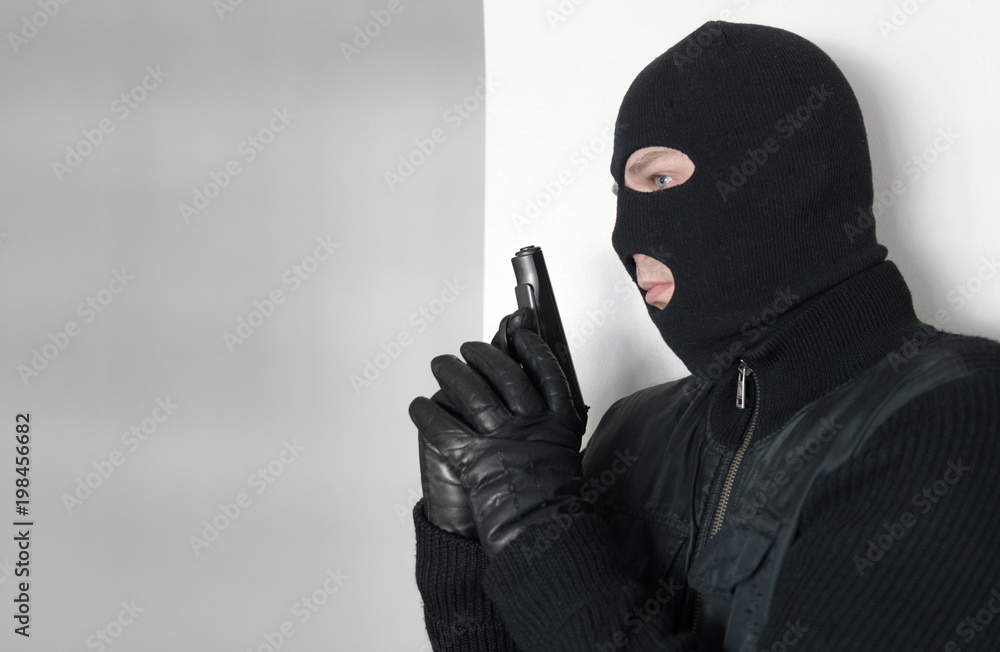 Armed man in balaclava hiding behind a wall. Armed man in balaclava hiding behind a wall.