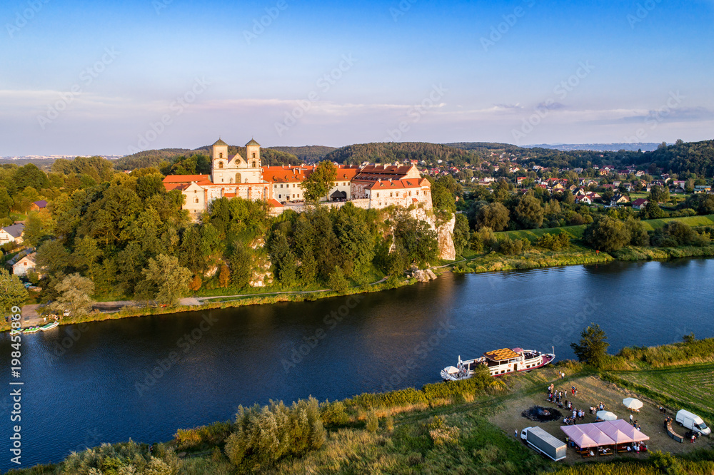 Tyniec near Krakow, Poland. Benedictine abbey, monastery and church on the rocky cliff, Vistula river, tourist ship and unrecognizable people enjoying the picnic at a bonfire and outdoor restaurant