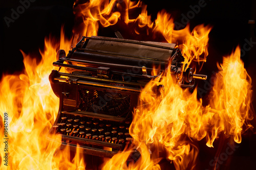 Concept shot of antique manual typewriter with paper burning on black background, selective focus