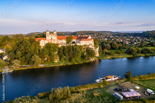 Tyniec near Krakow, Poland. Benedictine abbey, monastery and church on the rocky cliff, Vistula river, tourist ship and unrecognizable people enjoying the picnic at a bonfire and outdoor restaurant