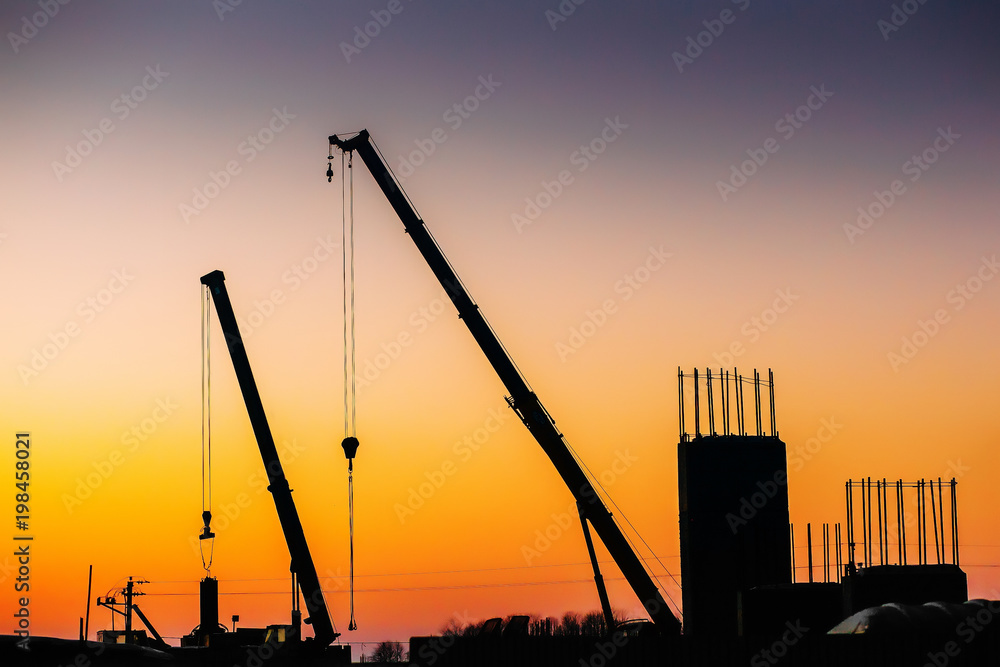 Crane and building construction site on background of sunset sky. Industrial landscape with silhouettes of cranes and building over evening sunlight. space for text