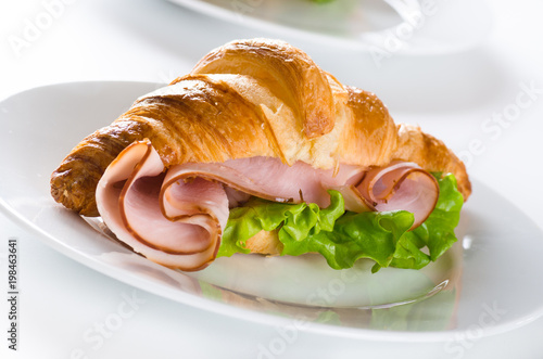 Fresh croissant with ham and salad leaf on white