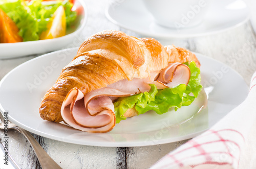 Fresh croissant with ham and salad leaf with sfresh salad on white wooden background
