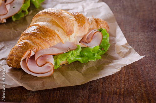 Fresh croissant with ham and salad leaf on dark wooden background