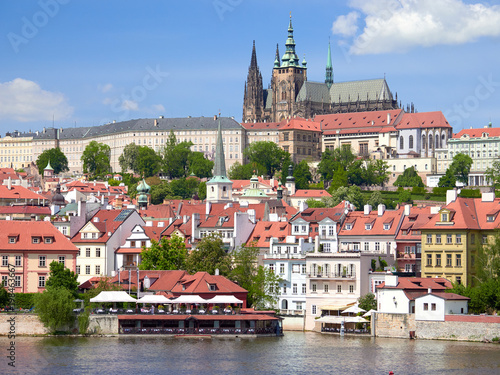 A riverside view of Vltava running through Prague with it's red rooftops on a sunny day in the Czech Republic.