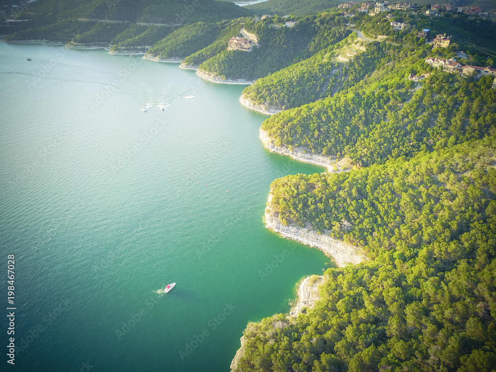 Naklejka premium Vintage aerial trees and cliff rock wall, bluffs at Lake Travis, Austin, Texas, USA. Luxury vacation homes and house on coastline. Looking down houses in community, boats, ocean crystal background