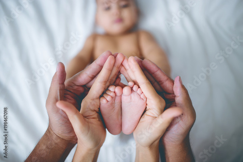 Hands of parents holds baby feet on the bed. photo