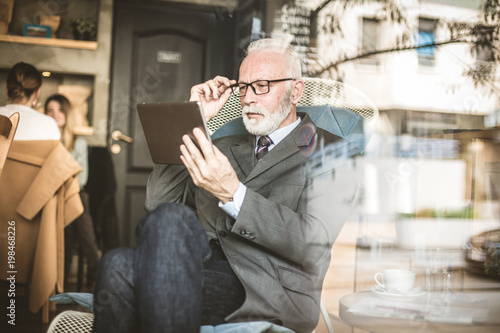 Senior businessman at cafe sitting and using digital tablet.