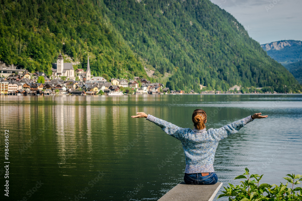 girl is sitting on wooden bridge. Young tourist woman sits on the bridge and enjoy the relaxation and freedom. Beautiful view of the mountain nature. wonderful view of Hallstatt. bridge over lake
