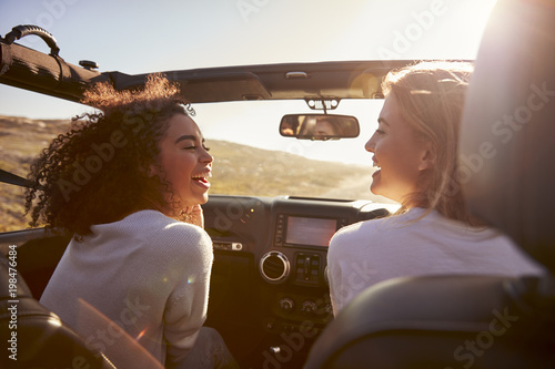 Two girlfriends driving with sunroof open look at each other photo
