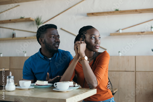 insulted african american woman with boyfriend sitting at table in cafe photo