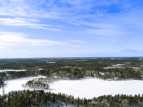 Aerial drone view of a winter landscape. Snow covered forest and lakes from the top. Sunrise in  nature from a birds eye view. Aerial photography. Aerial photo. Quadcopter. Winter road © Aleksei