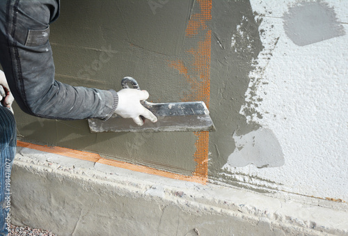 Contractor plastering wall with fiberglass mesh, plaster mesh after rigid insulation. Plastering house wall.