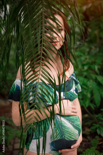 Beautiful pregnant caucasian redhead woman in swimsuit in palm l