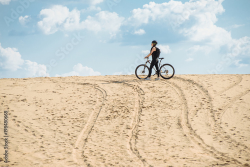 Female mountainbiker in desert. Fit sport woman wearing sportswear standing with her bicycle. Extreme games. Desert trip.