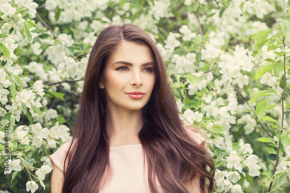 Fashion Portrait of Young Brunette Woman with Long Brown Hair and Makeup on Blossom Spring Flowers Background Fashion Portrait of Young Brunette Woman with Long Brown Hair and Makeup on Blossom Spring Flowers Background