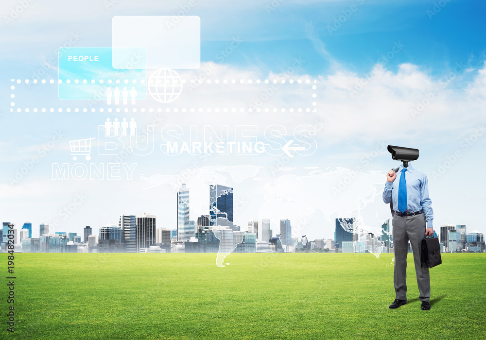 Camera headed man standing on green grass against modern cityscape