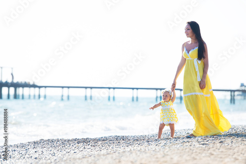 happy family in a yellow dress. Mother and child are walking on the beach