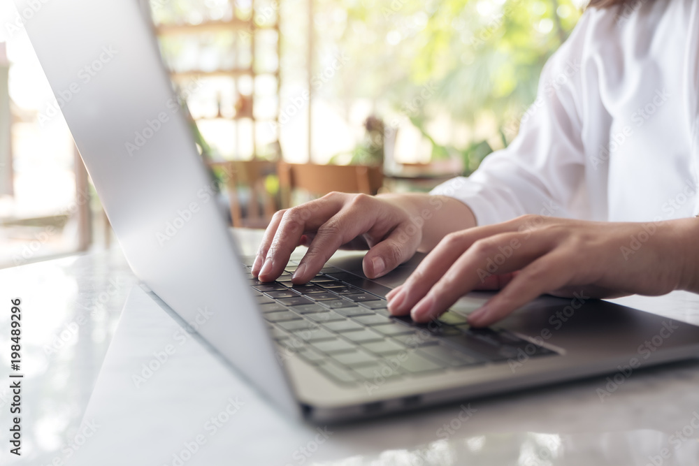 Closeup image of woman's hands working and typing on laptop keyboard on table with blur nature background Closeup image of woman's hands working and typing on laptop keyboard on table with blur nature background