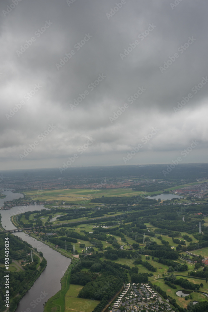 Farms in Holland, Netherlands with canal viewed from plane in sky with clouds