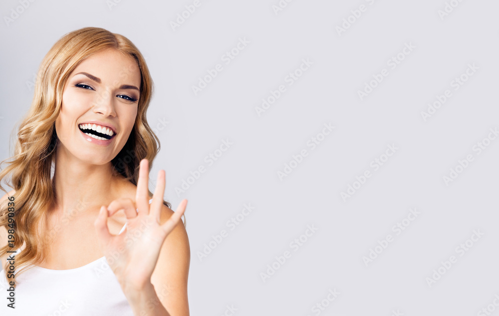 Young woman showing okay gesture, over grey Young woman showing okay gesture, over grey