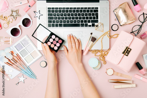 Fashion blogger working with laptop. Workspace with female accessory, cosmetics products on pale pink table. flat lay, top view