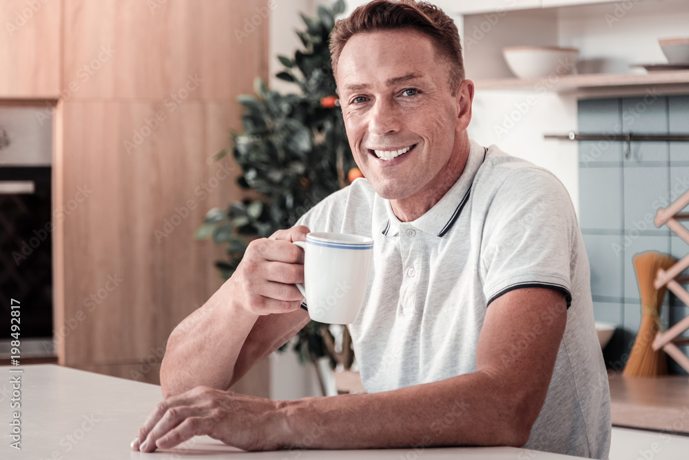 Morning relaxation. Joyful male expressing positivity while drinking tea and having good mood Morning relaxation. Joyful male expressing positivity while drinking tea and having good mood