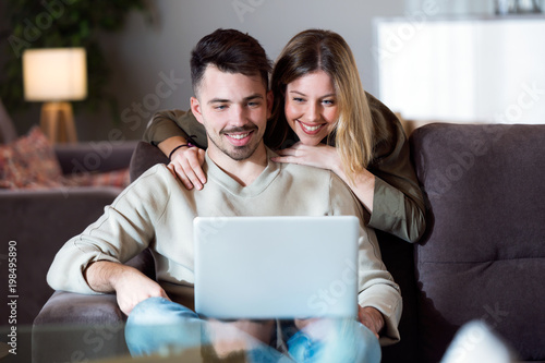 Beautiful young smiling couple using their laptop at home.