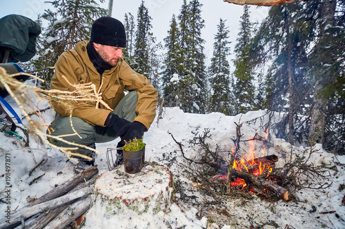 Male sitting by the fire and warms yourself over the fire in winter in the tundra forest