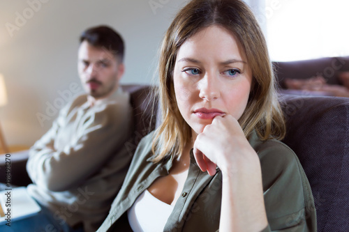 Offended young woman ignoring her angry partner sitting behind her on the couch at home.