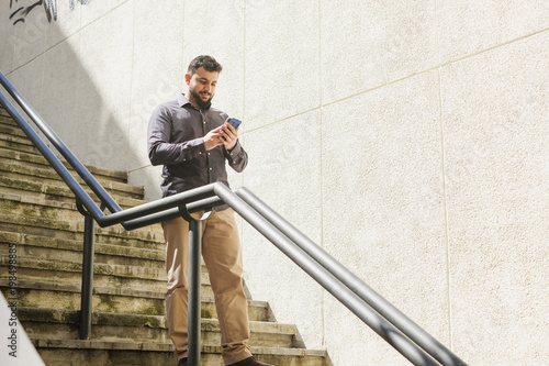 Obraz na plátně bearded man looking amartphone while walking down the stairs