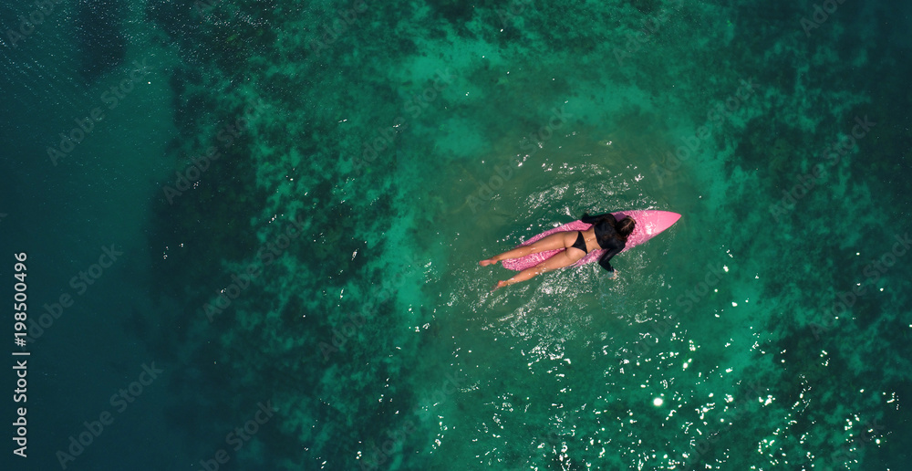 Fototapeta premium Aerial top view of beautiful young woman in swimsuit with pink surfboard enjoying her holiday in amazing clear sea water