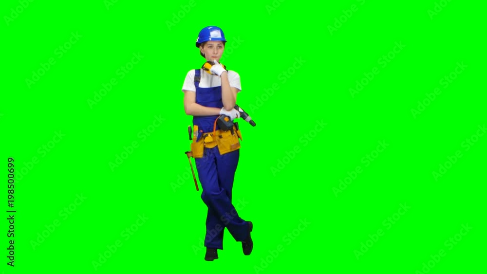 Builder girl in a helmet and overalls holds a drill in her hands . Green screen Builder girl in a helmet and overalls holds a drill in her hands . Green screen