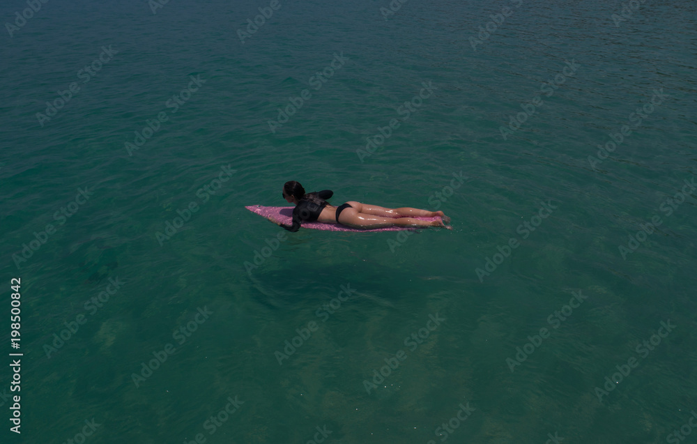 Aerial drone view of beautiful young woman in swimsuit and sunglasses with pink surfboard enjoying her holiday in amazing clear sea water
