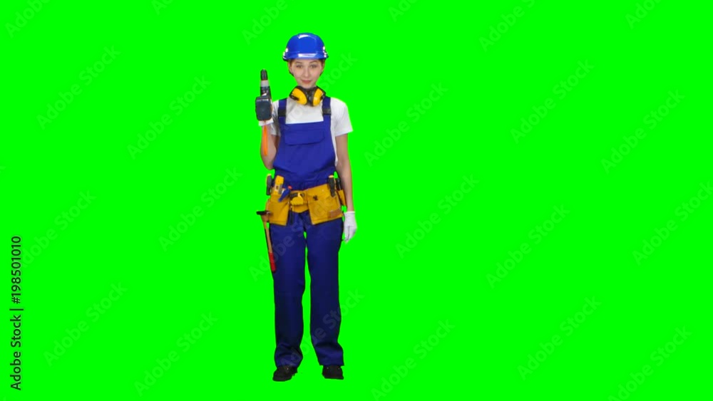 Engineer girl in a helmet and overalls holds a drill in her hands . Green screen Engineer girl in a helmet and overalls holds a drill in her hands . Green screen